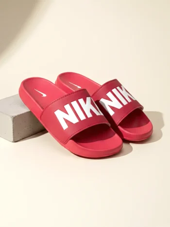 Red slip-on slide footwear with a wide strap featuring bold white lettering, displayed in a minimal studio setup with a soft neutral background.
